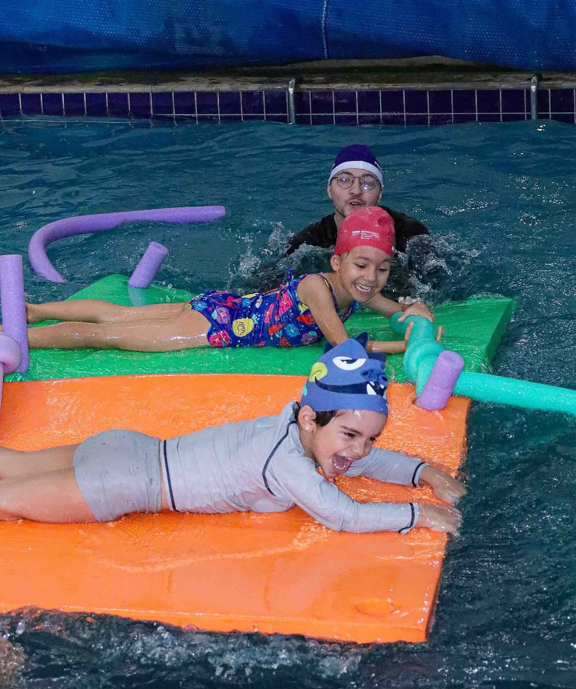 Bebês em pranchas de isopor na piscina aquecida